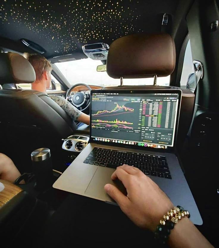 a man sitting in the back seat of a car using a laptop computer