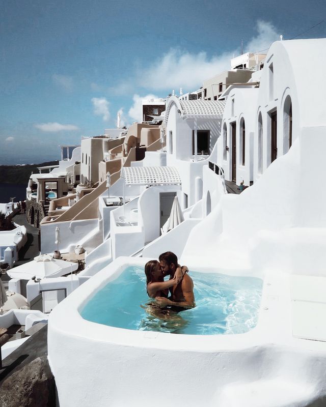 two people in a hot tub on the roof of a building with white walls and balconies