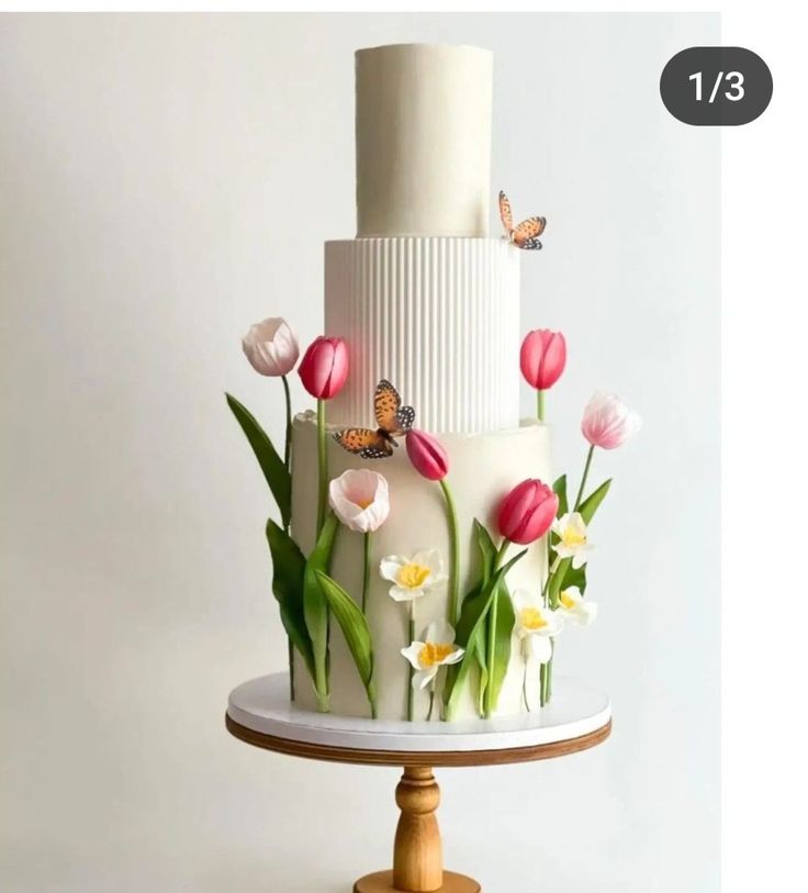 a three tiered cake with flowers and butterflies on the top is decorated in white icing