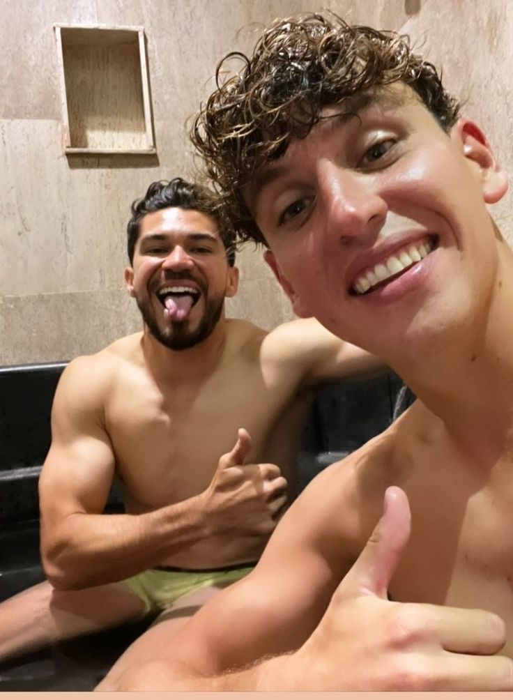 two men sitting in a bathtub with one giving the thumbs up and smiling at the camera