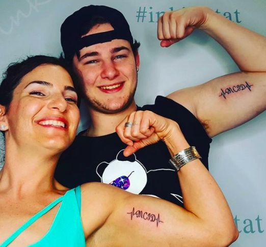 a man and woman with tattoos on their arms posing for a photo in front of a wall