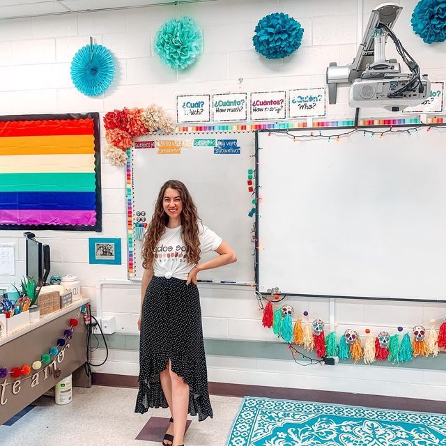 a woman standing in front of a whiteboard with many colors on it and decorations around her