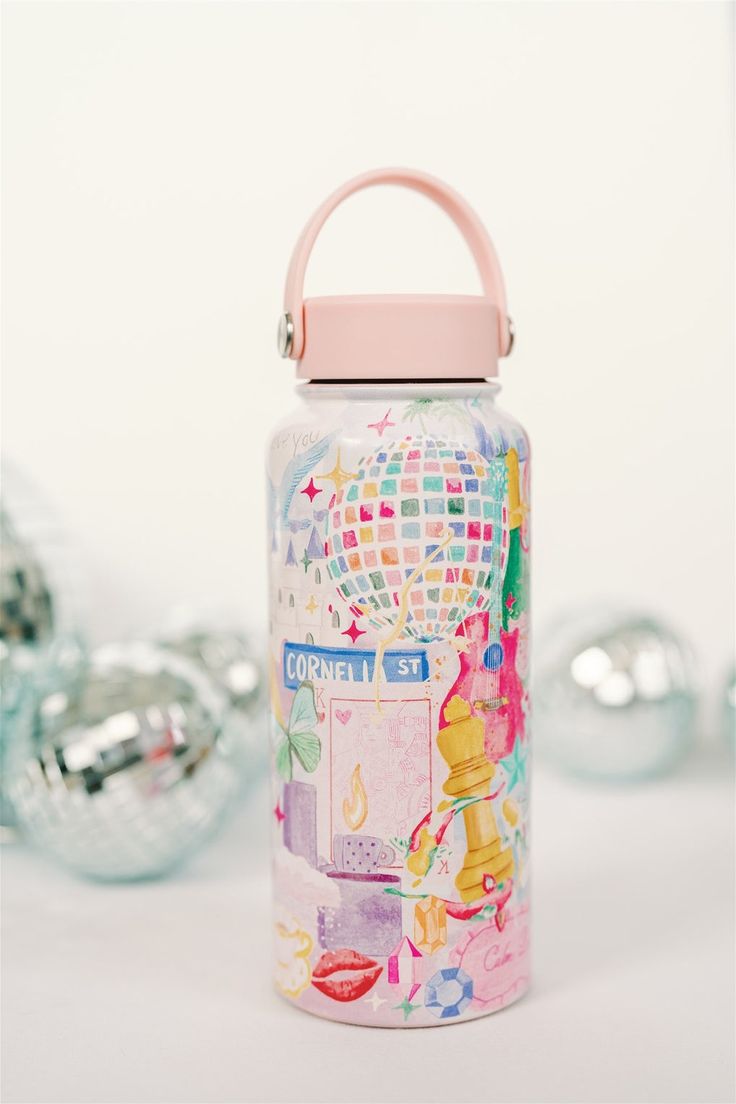 a water bottle with a pink lid and handle sitting on a table next to silver ornaments