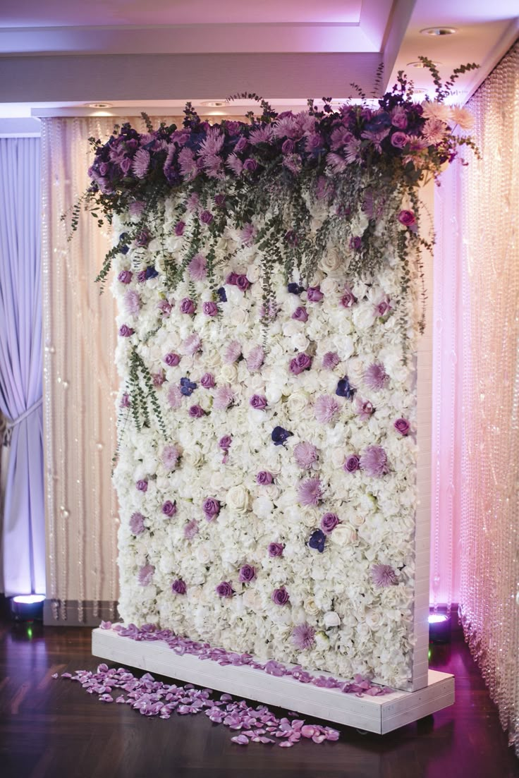 a flower covered wall with purple and white flowers on the side, along with petals