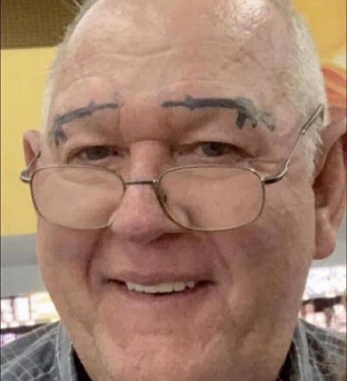 an older man with eyeliners on his forehead smiles at the camera while wearing glasses