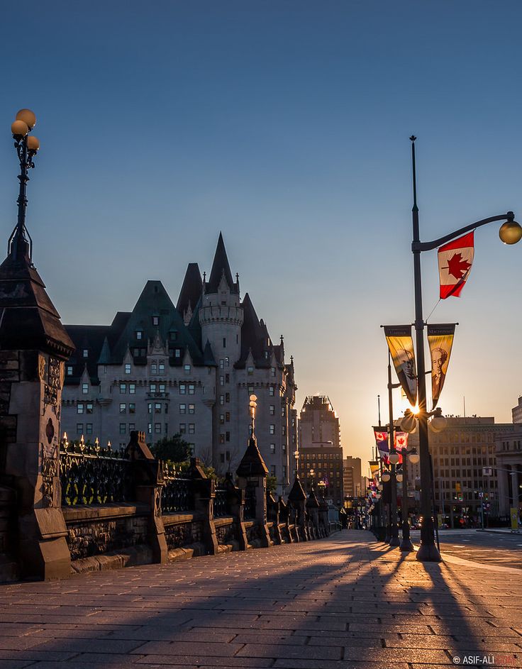 the sun is setting over a city with tall buildings and flags flying in the wind