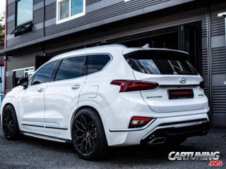 the rear end of a white car parked in front of a building with black rims