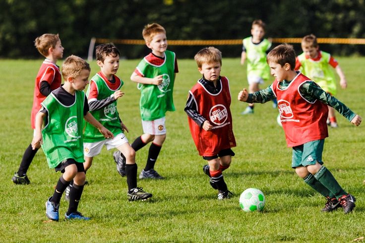 young boys playing soccer on a field with green grass and trees in the back ground