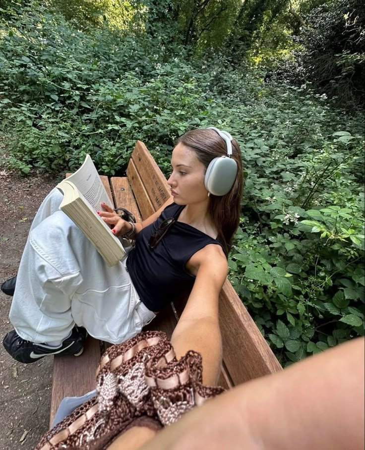 a woman with headphones sitting on a bench reading a book