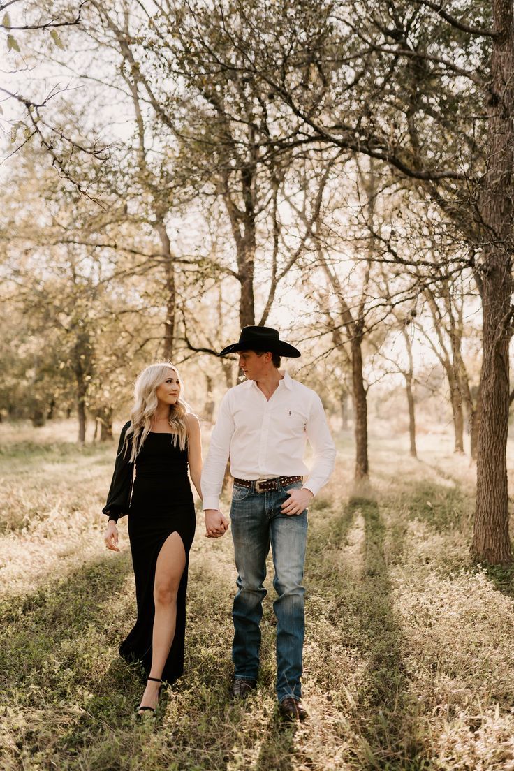 a man and woman holding hands while walking through the grass with trees in the background