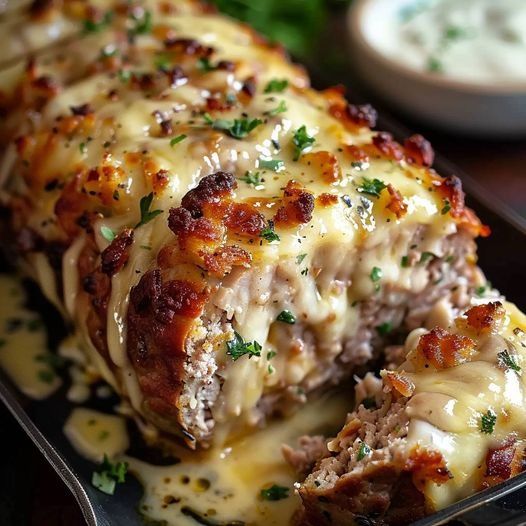 meatloaf covered in melted cheese and parsley on a black platter with sauce