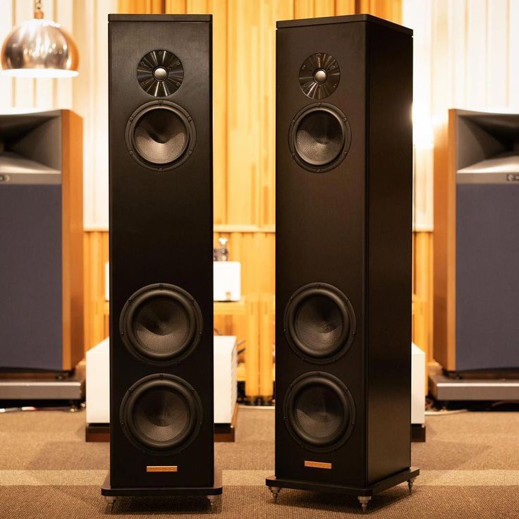 two black speakers sitting next to each other in front of a wall mounted speaker system