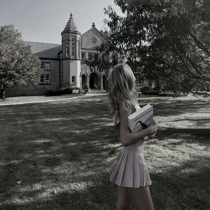 a girl in a pink dress is holding a book and looking at the building behind her