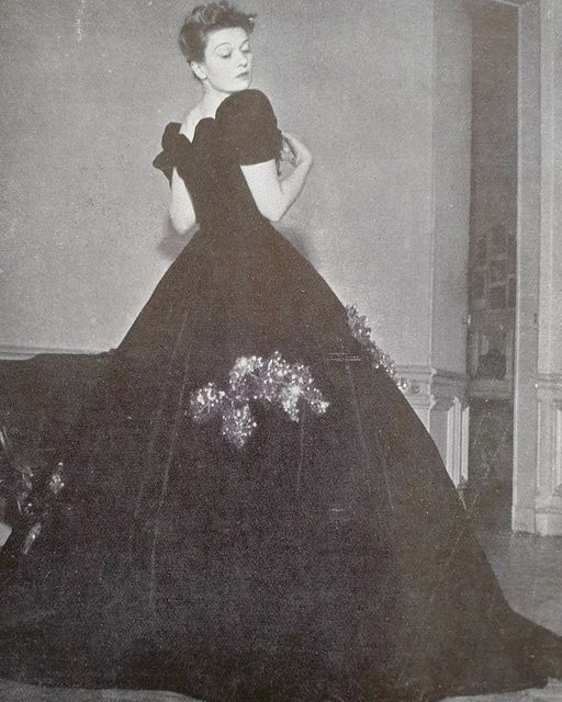 an old fashion photo of a woman in a black dress with flowers on the skirt