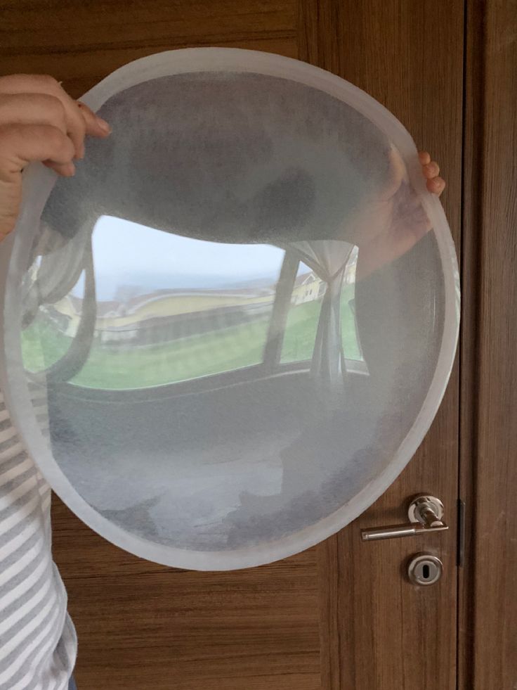 a person holding up a large round object in front of a door with the reflection of a golf course on it