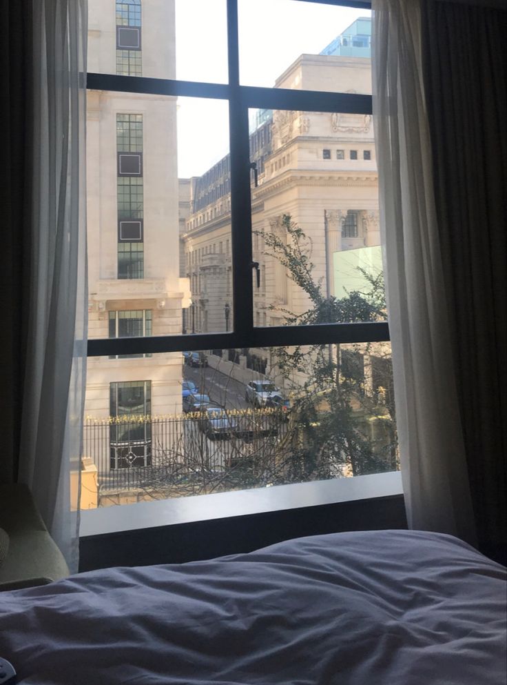 a bedroom with a large window looking out onto the street outside it and buildings in the distance