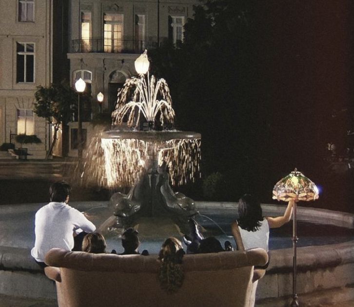 people are sitting on a couch in front of a fountain with fireworks coming from it