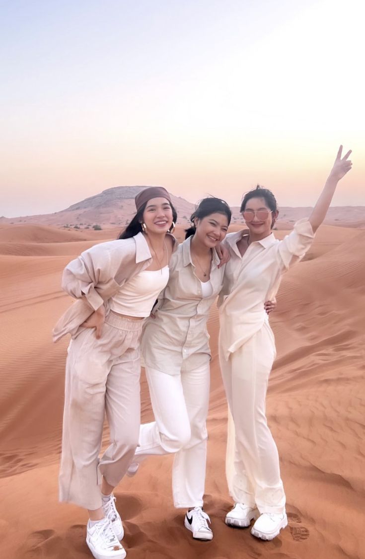 three women standing in the desert with their arms up and one holding her hand out