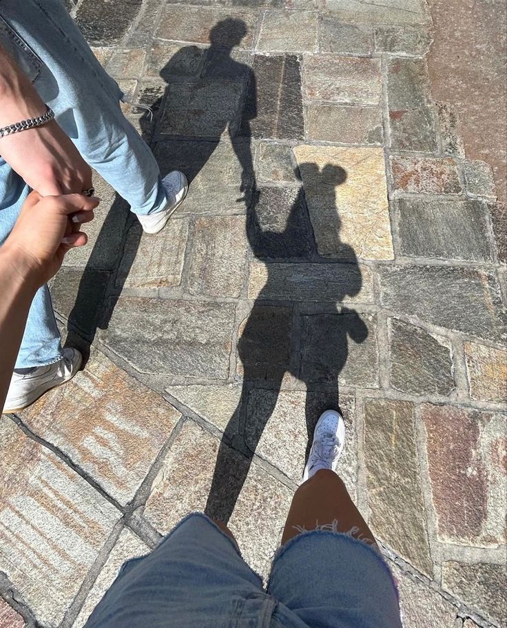 two people standing next to each other with their shadows on the ground