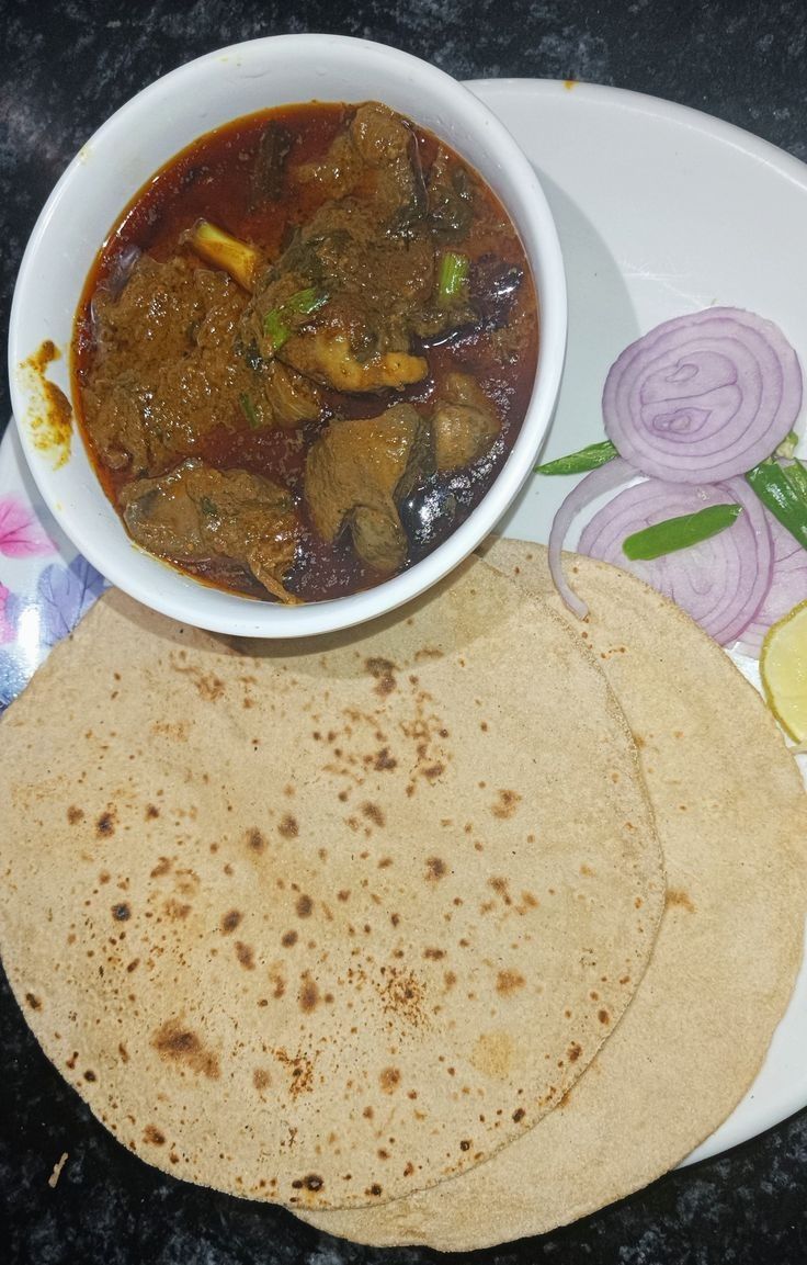 a white plate topped with two tortillas next to a bowl of soup and sliced onions