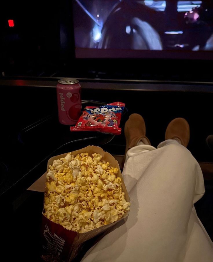 a person sitting in front of a television with popcorn and soda on the table next to it