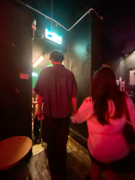 a man and woman are walking down the stairs in a dark room with neon lights