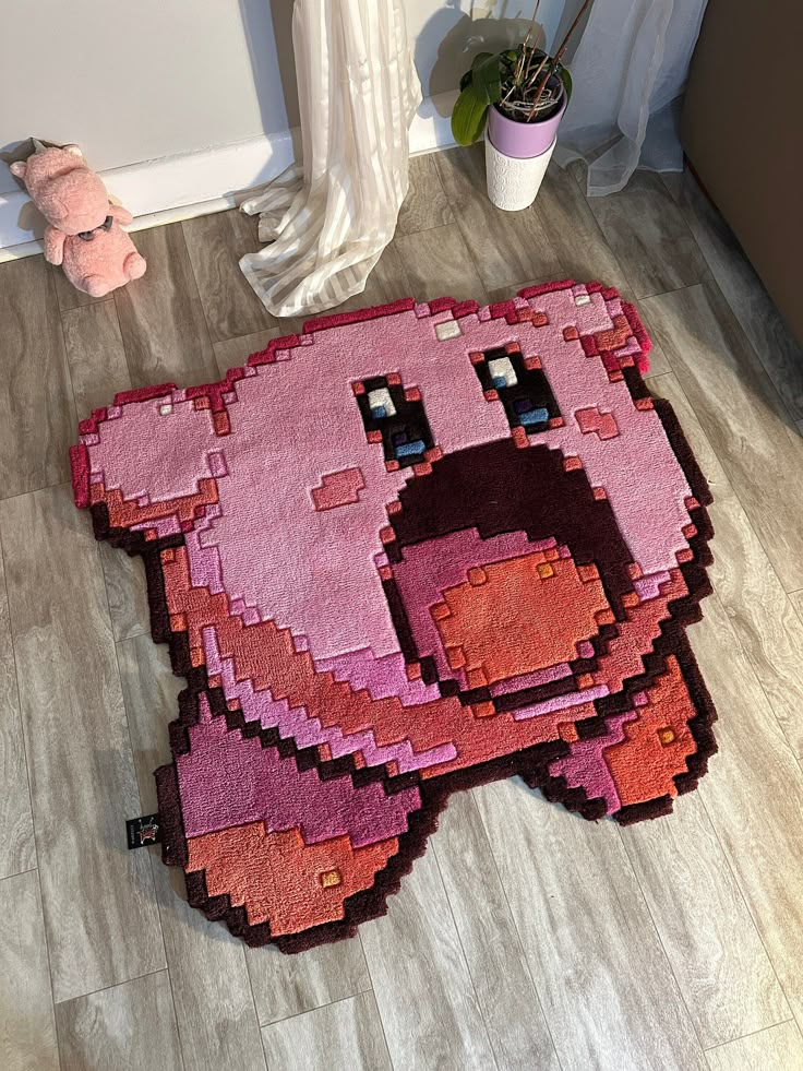 the rug is shaped like a pink pig with black eyes and nose, sitting on the floor next to a stuffed animal