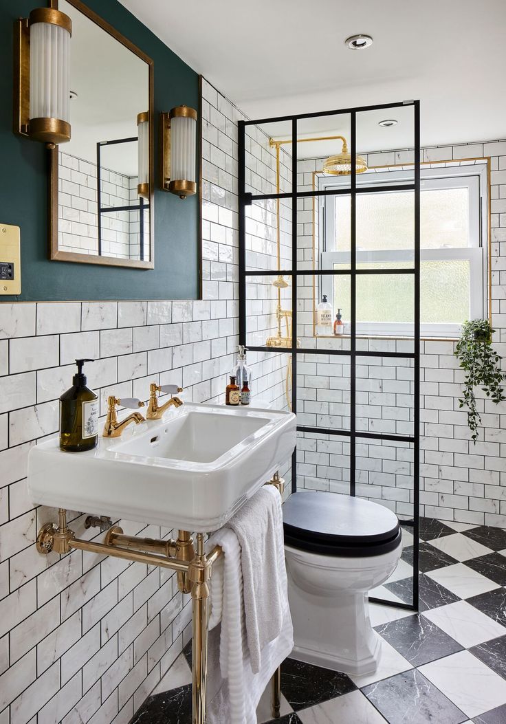 a white toilet sitting next to a sink in a bathroom under a mirror with gold fixtures