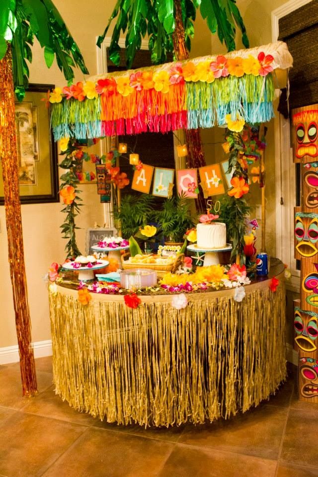 a table topped with lots of food and decorations next to two palm trees in the background