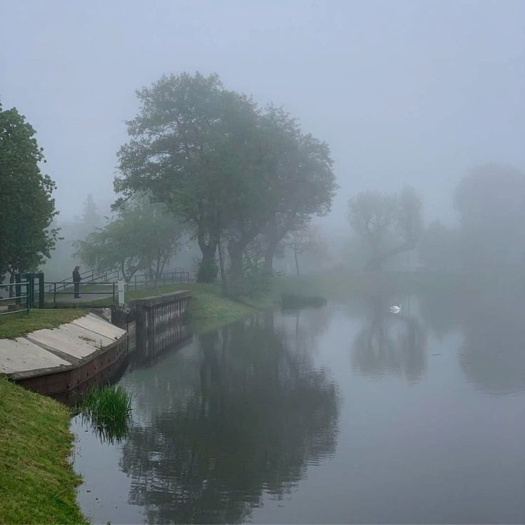 a foggy day on the water with boats in it and people walking along side