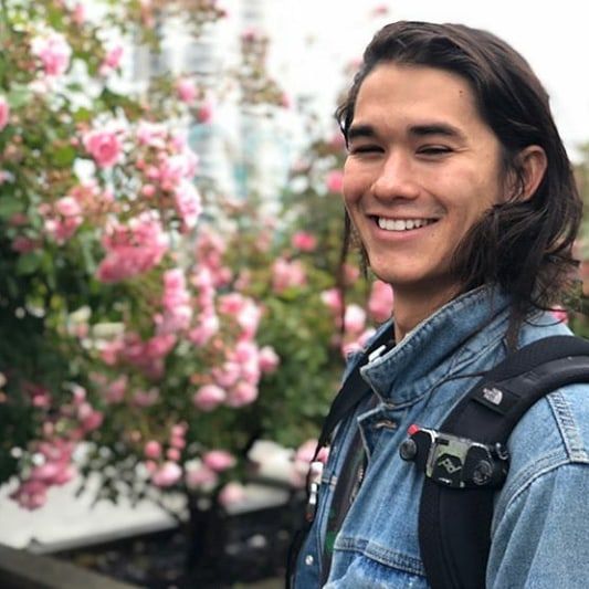 a young man is standing in front of some pink flowers and smiling at the camera