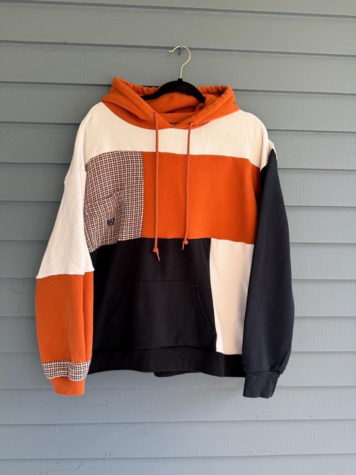 an orange, black and white hoodie hanging on a gray wall with blue siding