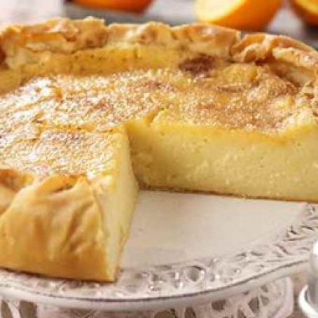 a pie sitting on top of a white plate next to an oranges in the background