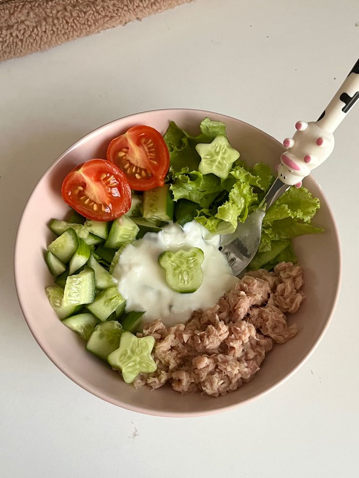 a white bowl filled with salad and dressing on top of a counter next to a knife