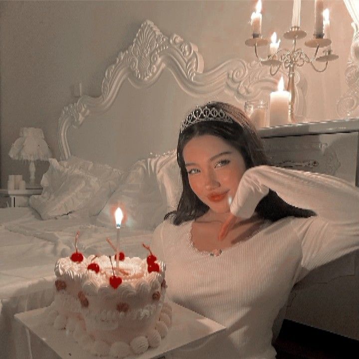 a woman sitting in front of a cake with lit candles on it and posing for the camera