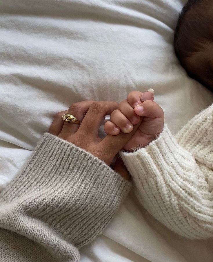 a woman laying in bed holding the hand of a baby