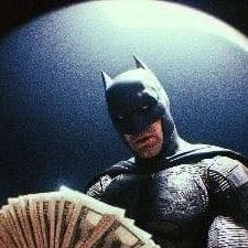 a man dressed as batman holding a fan and looking at the camera with money in front of him