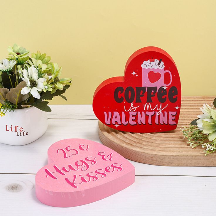 two heart shaped boxes sitting on top of a white table next to flowers and potted plants