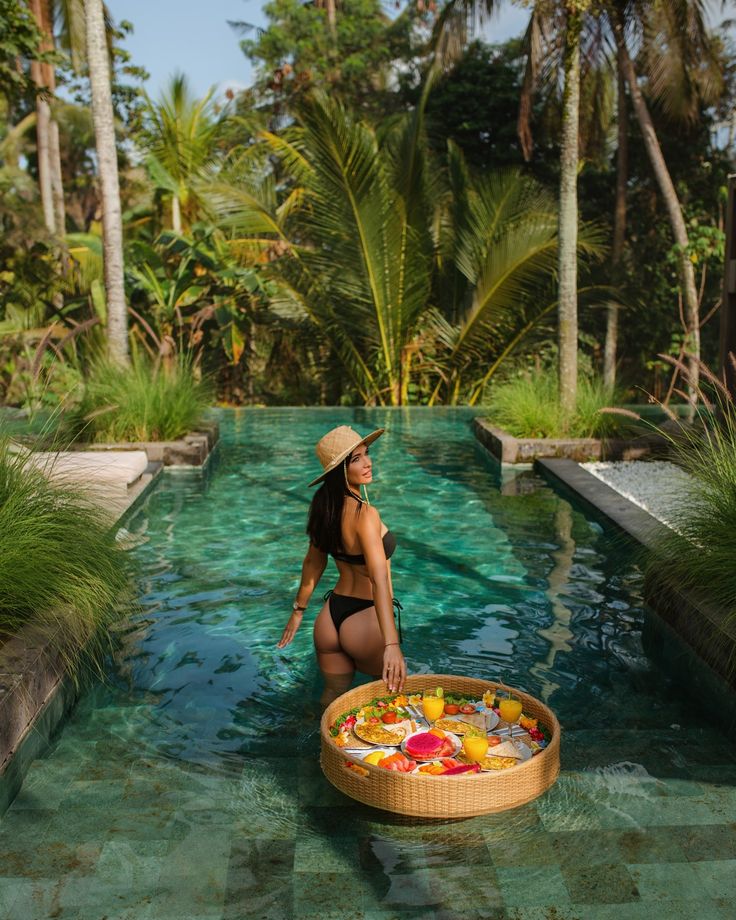 a woman in a bathing suit and straw hat sitting on the edge of a pool