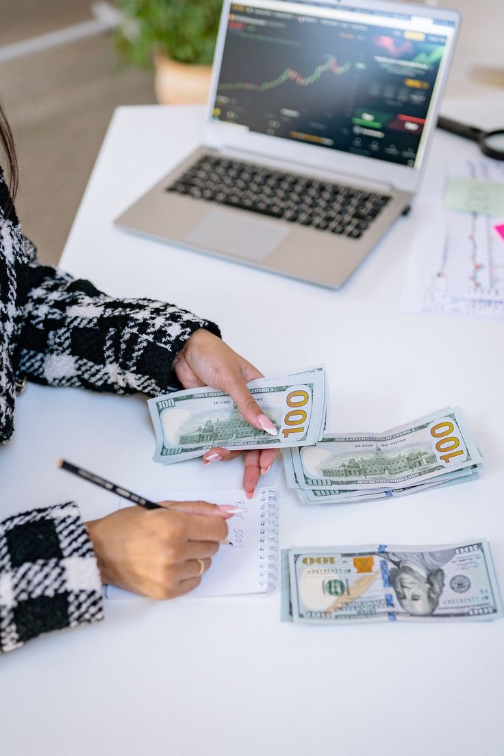 a woman sitting at a table with money in front of her and a laptop on the desk