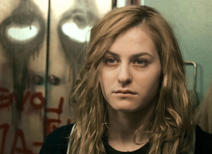 a woman with long blonde hair standing in front of a mirror looking at the camera