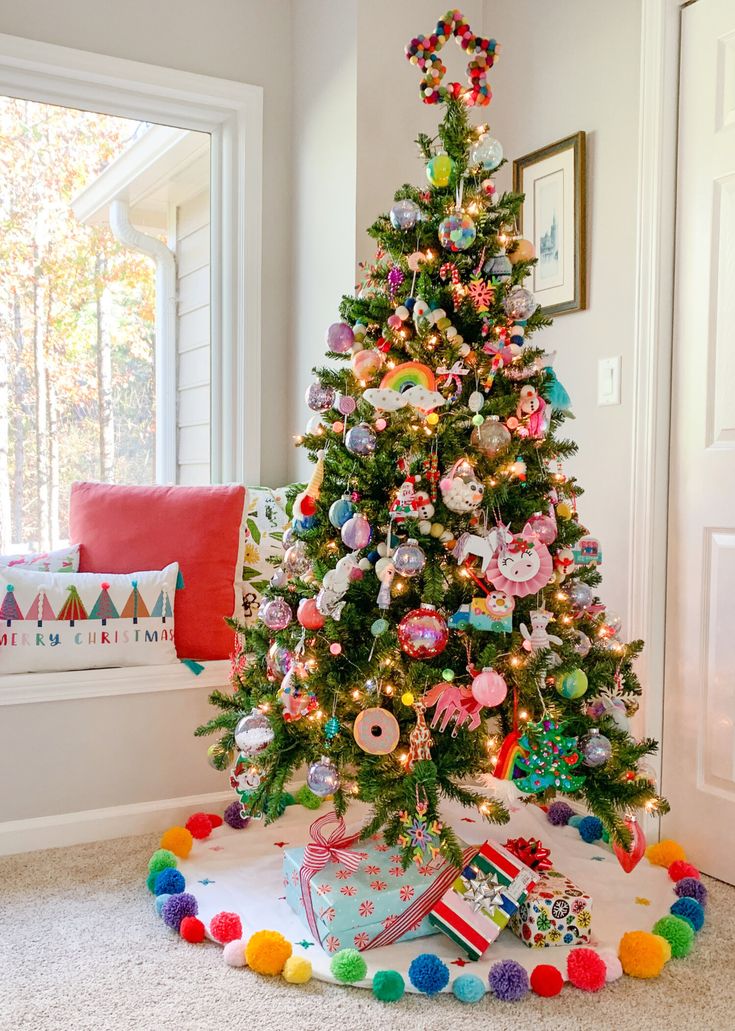 a brightly decorated christmas tree in the corner of a living room with pom - poms