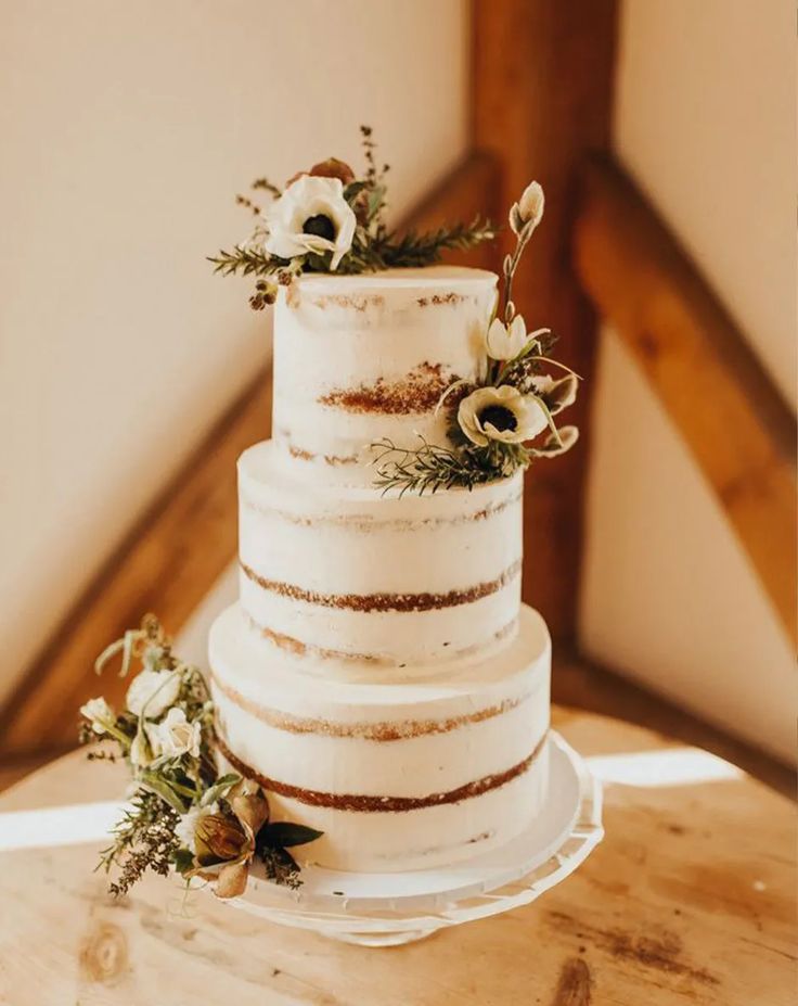 a three tiered wedding cake with flowers on the top is sitting on a wooden table