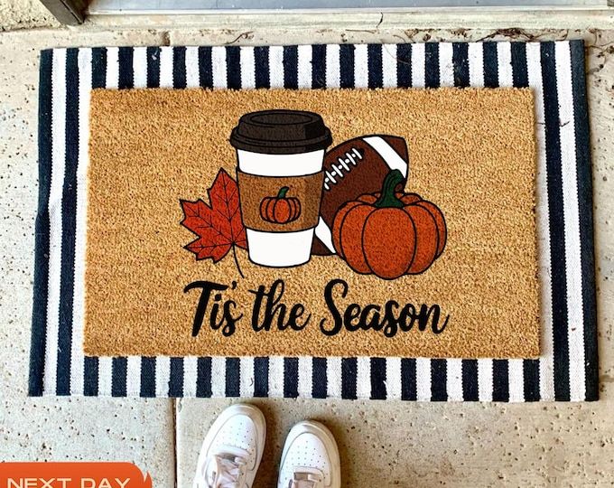 a door mat that says tis the season with a cup of coffee and pumpkins