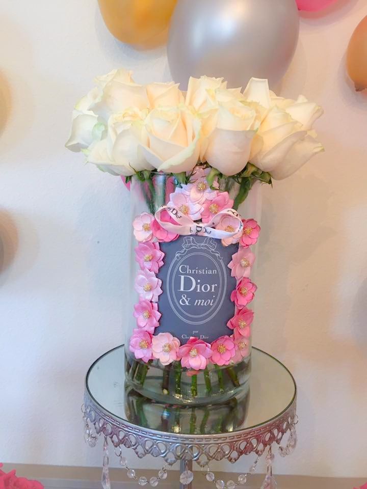 a vase filled with white and pink roses on top of a glass table next to balloons