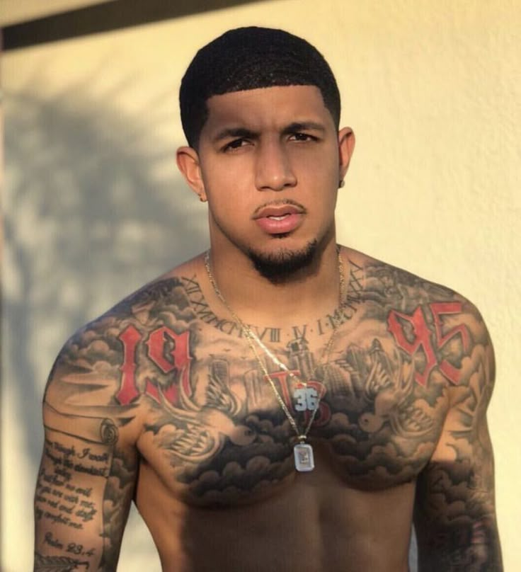 a man with tattoos on his chest standing in front of a building