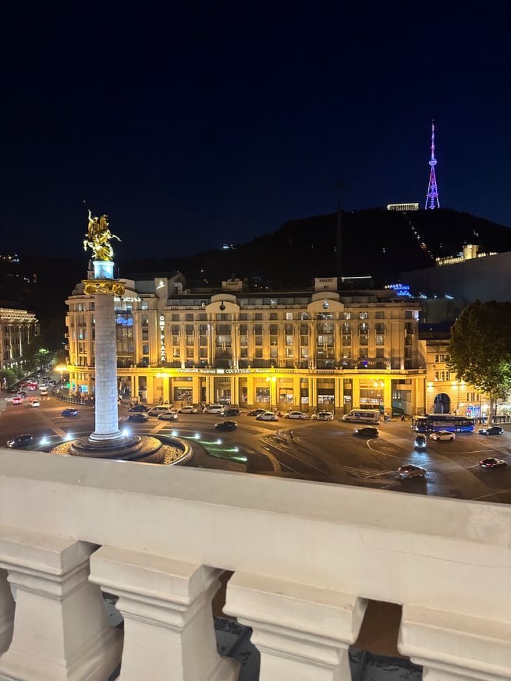 a view of a city at night from the top of a building with a statue on it