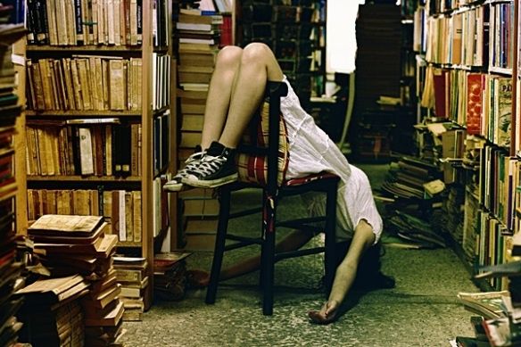 a person sitting in a chair with their legs up on a book shelf full of books