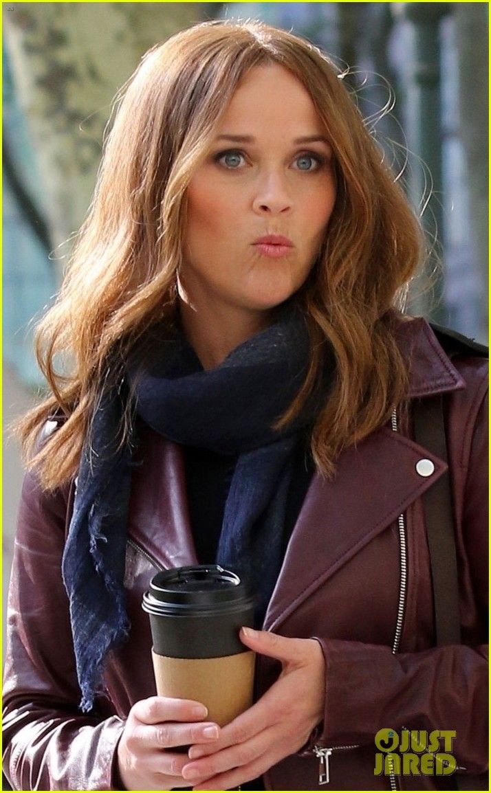 a woman holding a coffee cup and wearing a leather jacket with a scarf around her neck