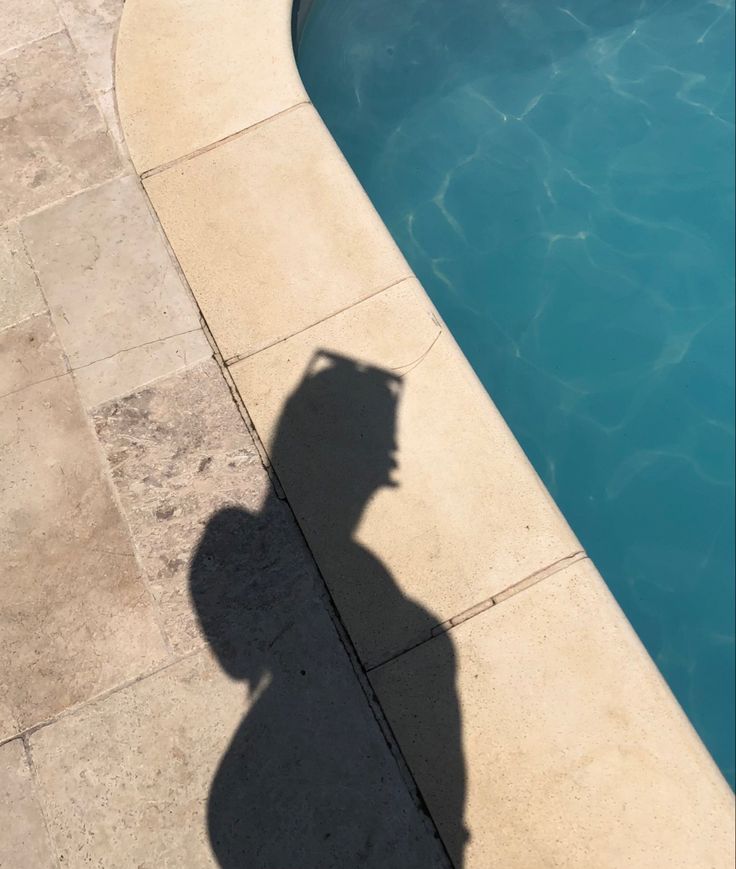 the shadow of a person standing next to a swimming pool